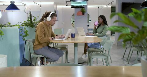 Remote professionals working opposite each other at communal table in pastel coworking space