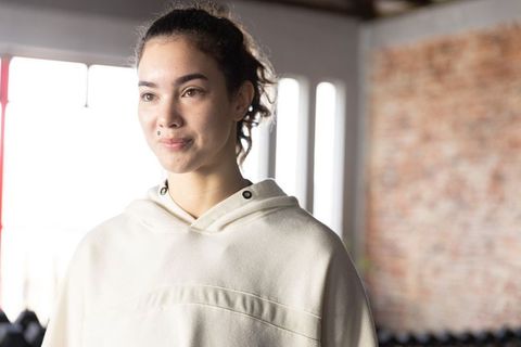Young woman wearing cream hoodie standing calm and confident in sunlit gym loft