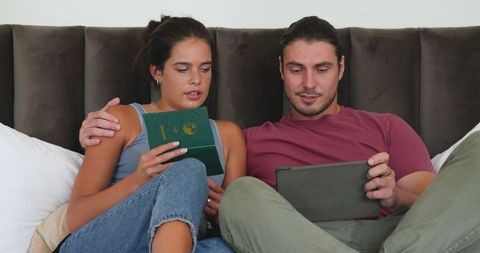 Couple Relaxing on Bed Using Tablet for Travel Planning