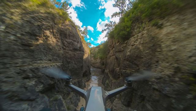Fpv quadcopter navigating narrow rocky canyon with motion blur, blue sky and sunlight