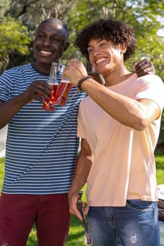 Diverse young men toasting with bottled drinks at backyard barbecue celebrating friendship