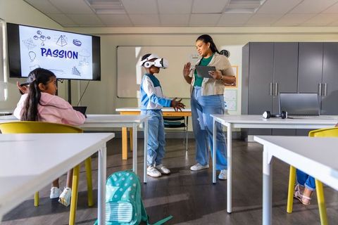 African american teacher guiding boy using vr headset in stem classroom
