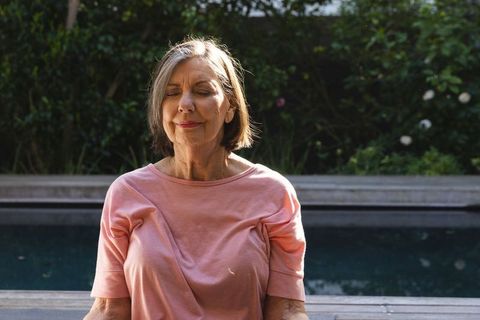Senior Woman Meditating by Tranquil Backyard Poolside