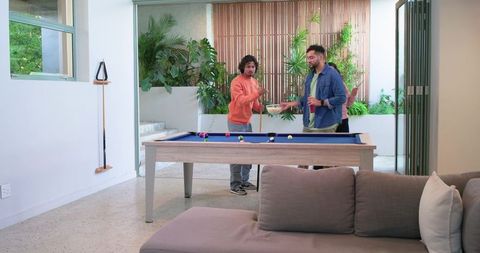 Friends enjoying game night playing pool and sharing snacks in modern living area