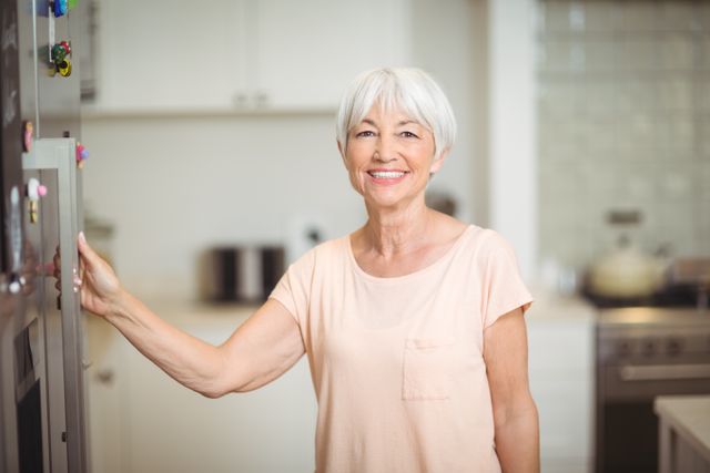 This image depicts a cheerful senior woman standing in a modern kitchen. She is smiling warmly, creating a welcoming and positive atmosphere. This image can be used for promoting healthy aging, lifestyle blogs, home and kitchen products, or senior living communities.