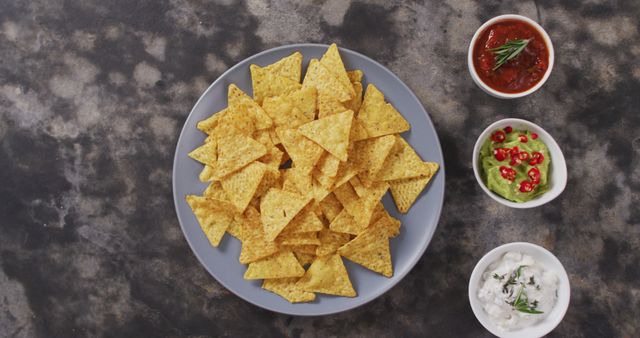 Plate of crispy nachos served with bowls of salsa, guacamole, and sour cream garnished with herbs. Ideal for illustrating Mexican cuisine, appetizer setups, party snacks, or food-related content in blogs, websites, or social media.