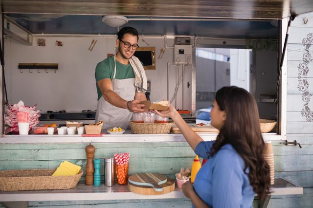 Food truck vendor serving a wrap to a customer. Ideal for use in articles about street food culture, small businesses, customer service, and urban dining experiences. Can be used in marketing materials for food trucks, culinary events, and outdoor dining promotions.