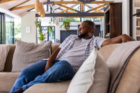 Relaxing on sunlit farmhouse sofa, african american man enjoying bright open-plan living