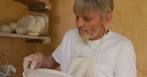Senior man inspecting pottery dish in workshop