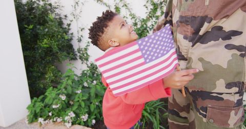 Child hugging military parent holding american flag outdoors