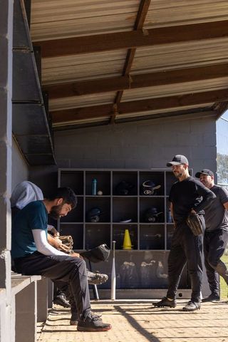 Sunlit dugout: players preparing and adjusting gloves while talking before baseball game