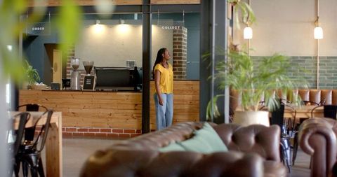 African american woman standing by wooden counter in rustic coffeehouse wearing yellow top