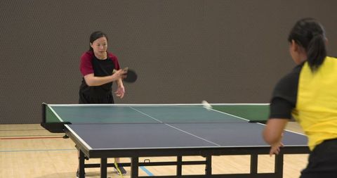 Competitive female table tennis match in gymnasium setting