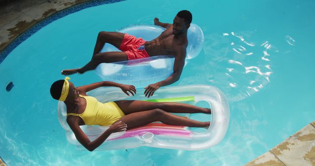 Happy african american couple lying on inflatables in swimming pool splashing each other and smiling. staying at home in isolation during quarantine lockdown.