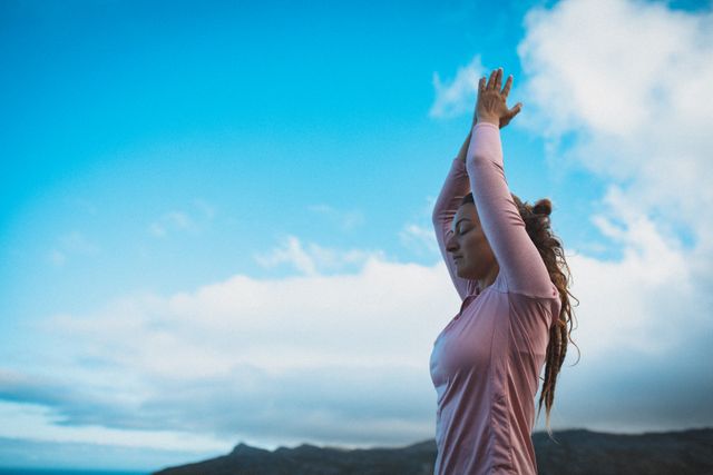 Caucasian woman practicing yoga and meditating in the mountains with a clear blue sky. Ideal for promoting wellness, mindfulness, outdoor activities, travel, and adventure. Perfect for use in lifestyle blogs, travel magazines, wellness websites, and advertisements focusing on relaxation and mental health.
