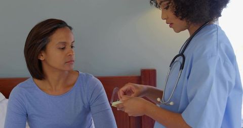 Nurse offering medication and instructions to patient on bed, gentle home healthcare visit