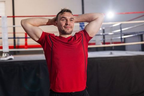 Confident male boxer resting in ring after intense training, standing with hands behind head
