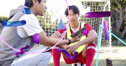 Coach showing tablet to teen soccer player on field during training with digital overlays