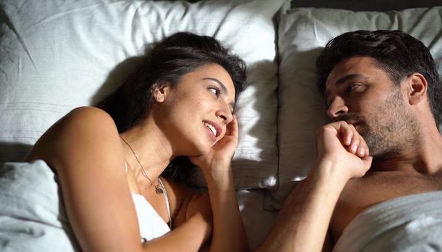 Intimate couple lying in bed smiling and talking, romantic nighttime bedroom scene, candid