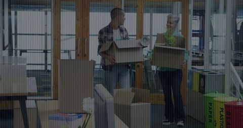 Coworkers carrying boxes during office move in open-plan workspace with recycling bins