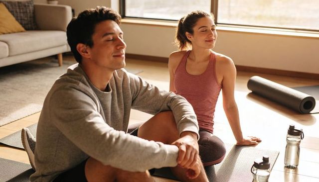 Young couple relaxing after yoga on living room mats in warm morning sunlight