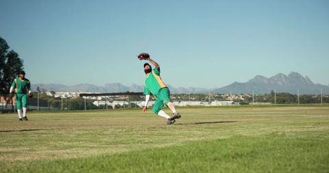 Male outfielder diving and reaching with glove during baseball game on sunny green field