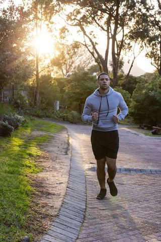 Man Jogging on Path Amidst Sunrise in Suburban Park