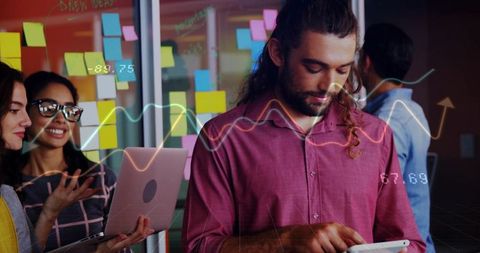 Man tapping tablet while colleagues brainstorming with sticky notes and data visualization