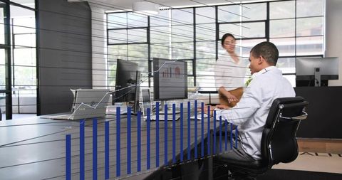 Businessman typing at monitor in modern open-plan office with financial bar-chart overlay