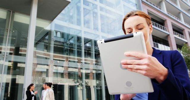 Focused caucasian businesswoman using tablet next to office building on sunny day - Download Free Stock Photos Pikwizard.com