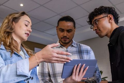 Diverse team collaborating over tablet in modern office, woman gesturing and explaining