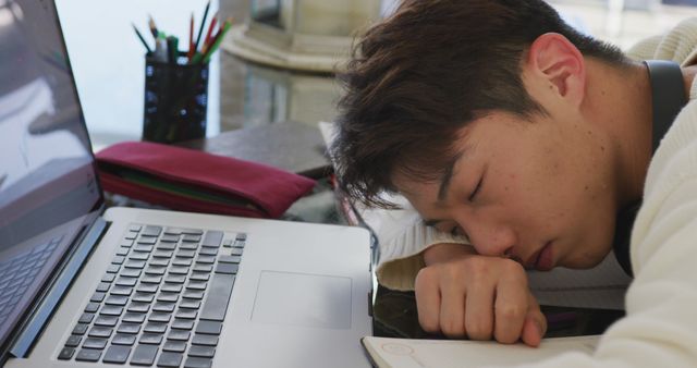 Asian male teenager with headphones sleeping and using laptop in living room. spending time alone at home.