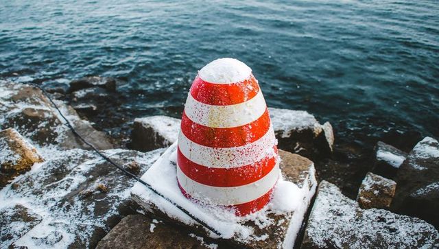 Resting red-and-white buoy on snow-covered breakwater at rocky shoreline