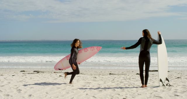 A young Caucasian woman and a girl stand on a sandy beach holding surfboards, with copy space. They appear to be preparing for a surfing session, enjoying the sunny weather and the vast ocean in front of them.