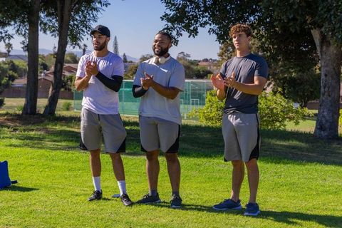 Multicultural male teammates clapping on sidelines during outdoor sports training