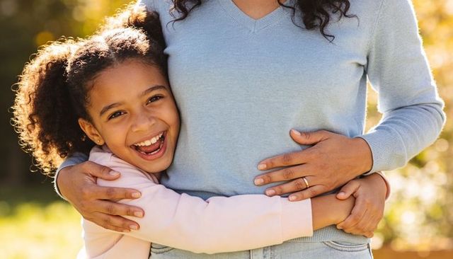 Joyful daughter hugging mother waist outdoors showing wedding band family togetherness