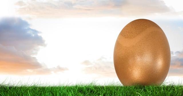 Golden Easter egg resting on green grass with a cloudy sky background. Ideal for Easter holiday promotions, celebration templates, seasonal social media posts, and festive greeting cards.