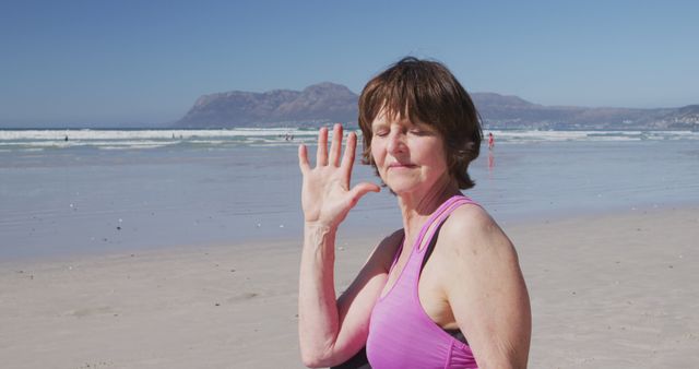 Portrait of caucasian senior woman waving on sunny beach. Yoga, fitness, healthy living, wellbeing and outdoor activities, unaltered.
