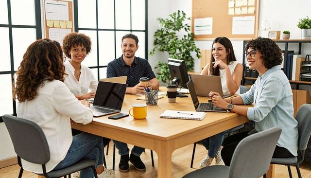 Diverse team collaborating around table with laptops in modern coworking office