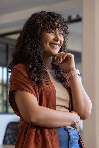 Smiling young woman wearing smartwatch and rust shirt standing confidently in modern office