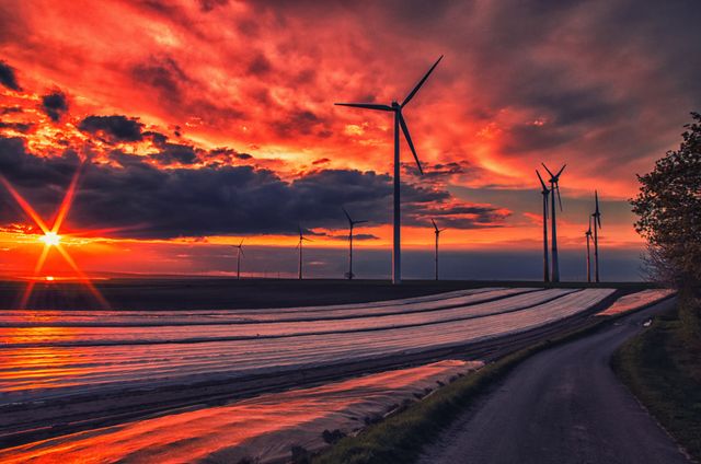 Wind turbines in countryside with dramatic sunset sky. Renewable energy source concept ideal for use in sustainability campaigns, environmental reports, and agricultural technology advertisements.