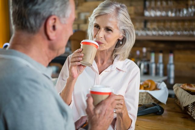 Senior couple enjoying coffee in a cozy café, engaging in conversation and bonding. Ideal for use in lifestyle, retirement, and social interaction themes. Perfect for promoting senior living, leisure activities, and coffee shop atmospheres.