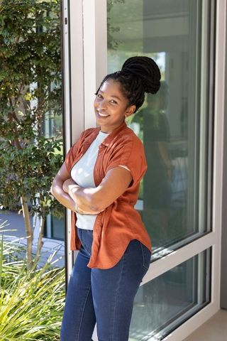 African woman leaning confidently against glass doorframe smiling in sunlit urban entrance