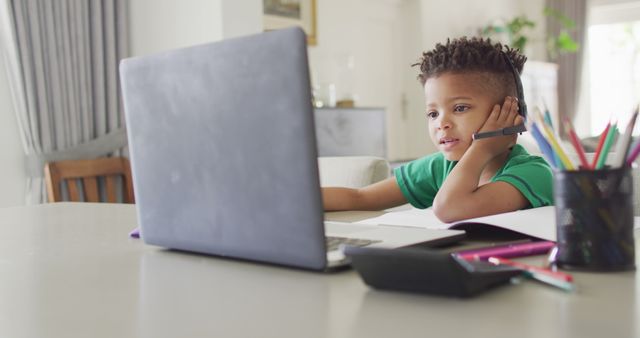 Happy african american boy sitting at table, using laptop for online lesson. Spending quality time at home, childhood, education and learning concept.