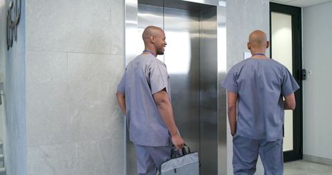 African american male nurses standing by elevator in hospital corridor wearing scrubs