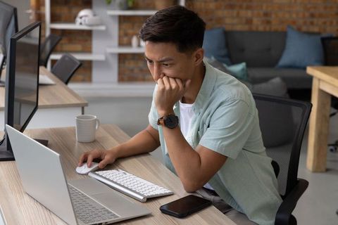 Focused asian male working on laptop in modern co-working office