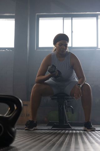 African american woman lifting dumbbell on bench in industrial gym, strength training