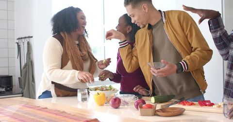 Diverse friends preparing fresh salad and laughing at bright modern kitchen island