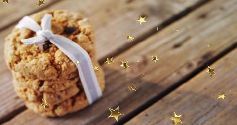 Displaying stacked oatmeal cookies tied with pale ribbon on wooden tabletop with gold stars
