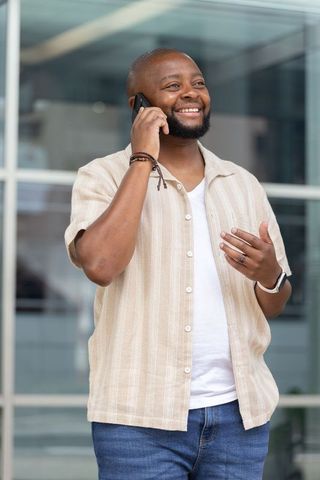 Smiling african man talking on smartphone outside modern office building, casual style